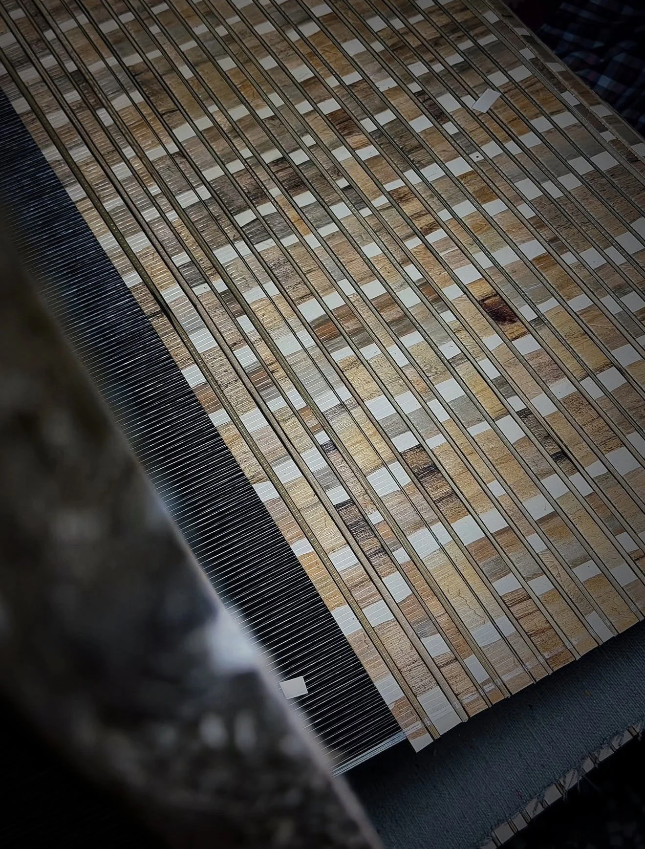 Close-up of a brown and pale patchwork surface beneath fine parallel threads during production