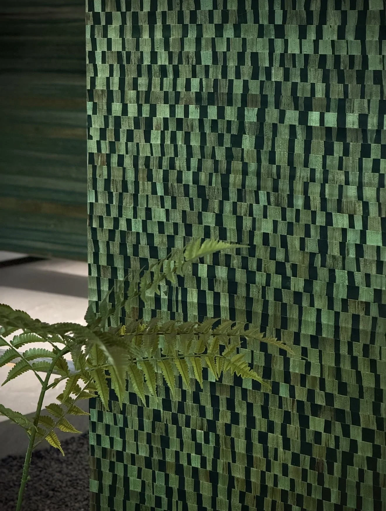 Green wallcovering with alternating textured rectangular forms and a fern in the foreground